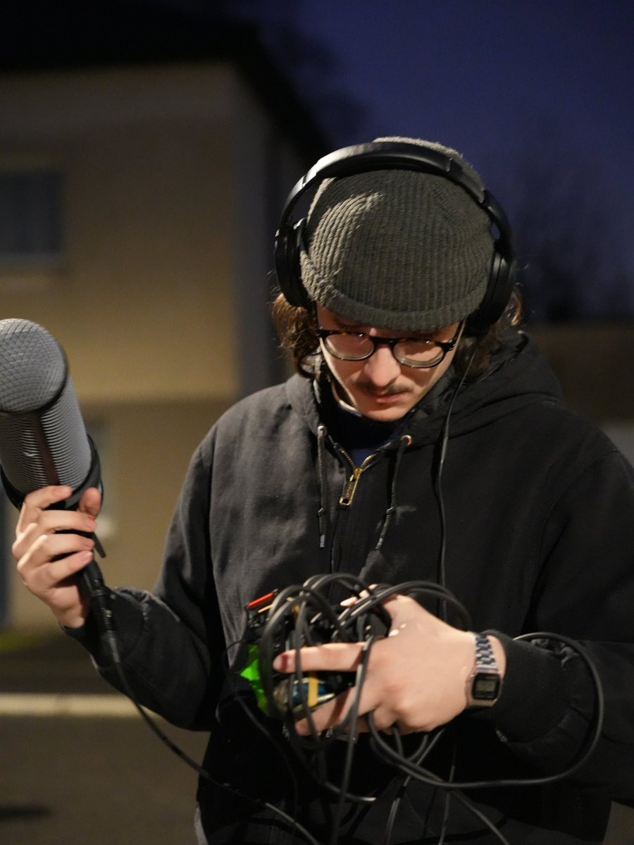 Ethan au casque, perche micro et câbles en main sur un tournage